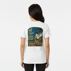 A woman viewed from behind wearing an Aretis white short-sleeve T-shirt with a large rectangular graphic print on the back. The print shows a retro-style beach scene with a woman riding a bicycle and the text 'all you need is less'.